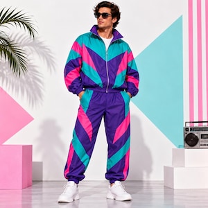 Può includere: Una tuta coordinata caratterizzata da un vivace motivo a blocchi di colore in viola, verde acqua e rosa acceso. La giacca presenta un colletto alto e una cerniera frontale, mentre i pantaloni hanno un elastico in vita e polsini alle caviglie.