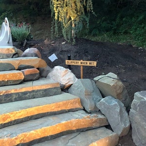 May include: Stone steps leading up a hill with a wooden sign that reads "SLIPPERY WHEN WET".