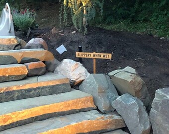 May include: Stone steps leading up a hill with a wooden sign that reads "SLIPPERY WHEN WET".