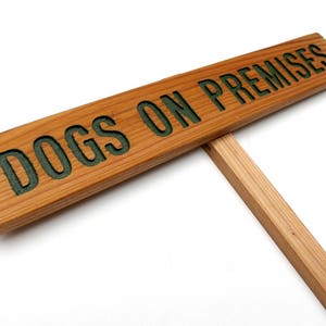 May include: A wooden sign with the text "DOGS ON PREMISES" in green letters. The sign is attached to a wooden stake.