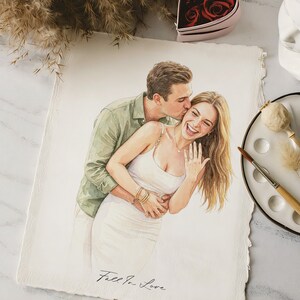 May include: A watercolour painting on textured paper depicting a person in a green shirt kissing the cheek of a person in a white dress who is laughing and showing a ring on their finger. The text Fall In Love is written at the bottom.