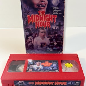 May include: A red VHS tape of the movie The Midnight Hour with a matching movie case. The tape features a label with the film title, a yellow Be Kind Please Rewind sticker, and a Blazin Video logo. The case cover shows a vampire and a group of people.
