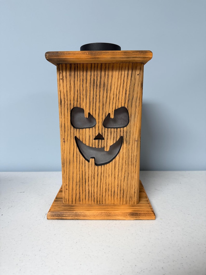 May include: A wooden jack-o'-lantern lantern with a black top and a cutout face. The lantern is stained in a light brown color and has a distressed finish.