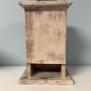 May include: A rustic wooden box with a distressed finish. The box has a small opening on the front and a black top.