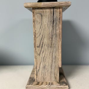 May include: A wooden box with a distressed gray finish. The box has a simple design with a flat top and a rectangular base. The box is made of wood with a visible grain pattern.
