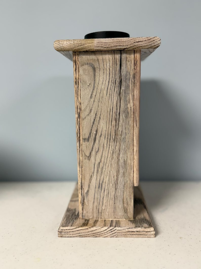 May include: A wooden box with a distressed gray finish. The box has a simple design with a flat top and a rectangular base. The box is made of wood with a visible grain pattern.