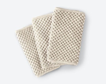 May include: Three rectangular off-white towels featuring a raised, textured bobble or popcorn knit pattern. Each towel has a finished hemmed edge and a consistent, uniform light cream color throughout the entire woven fabric surface.