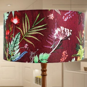May include: A floor lamp with a wooden base and a red lampshade with a floral print. The lampshade features a variety of green leaves and flowers in shades of pink, purple, and blue.