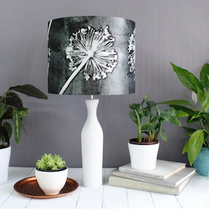 May include: A white table lamp with a gray and white floral patterned lampshade. The lamp is on a white table with books and plants.