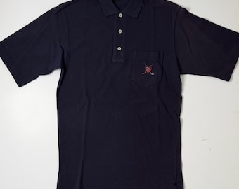 Puede incluir: Un polo de manga corta azul marino con cuello, tapeta de tres botones y un bolsillo en el pecho. El bolsillo muestra un escudo bordado con palos de golf cruzados y el texto Polo by Ralph Lauren en la etiqueta del cuello.