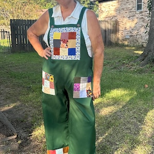 May include: Dark green overalls featuring a square patchwork bib panel with various fabric squares, two large patchwork pockets on the front, and a wide patchwork hem at the bottom of each leg. The overalls are worn over a white sleeveless collared shirt.