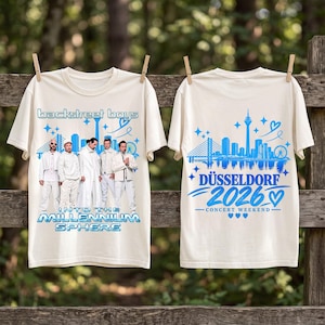Puede incluir: Una camiseta color crema con un gráfico azul de los Backstreet Boys y el texto "Into the Millennium Sphere" al frente, y un gráfico azul del horizonte de Düsseldorf con el texto "Düsseldorf 2026 Concert Weekend" en la parte posterior.