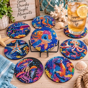 May include: A set of seven round coasters featuring colorful diamond art designs of sea creatures, including a turtle, starfish, octopus, and jellyfish. The coasters are displayed with a glass of iced tea and a sign reading Good Drinks Bright Moments.