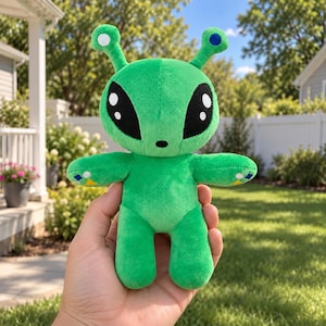 Op de afbeelding: Een felgroen pluche alien-speeltje met een groot hoofd en twee antennes, elk bekroond met een klein rond accent. De alien heeft extra grote, amandelvormige zwarte ogen met witte accenten en kleine gele en blauwe details op de handen.