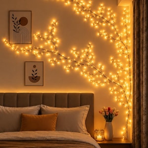 May include: A decorative branch-shaped string light with numerous small, warm-toned LED bulbs arranged in a sprawling, organic pattern across a wall, creating a soft, ambient glow that illuminates the space above a bed and framed wall art.