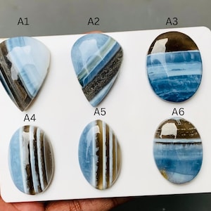 May include: Six polished blue and brown banded gemstones arranged on a white card. The stones are labeled A1 through A6 and feature distinct horizontal or diagonal stripes of light blue, dark brown, and white in oval and teardrop shapes.