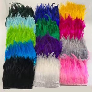 May include: A collection of feather trim strips arranged in a grid, featuring a variety of vibrant colors including black, blue, lime green, light blue, dark green, purple, white, yellow, magenta, grey, and pink, each attached to a fabric tape.