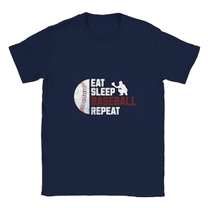 May include: A navy blue short-sleeved t-shirt featuring a graphic on the chest. The design includes a white baseball, a silhouette of a baseball catcher, and the white and red text that reads EAT SLEEP BASEBALL REPEAT in a distressed style.