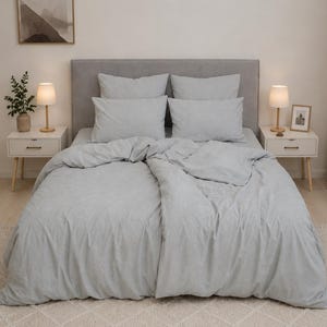May include: A light gray bedding set featuring a duvet cover and four matching rectangular pillows arranged on a bed with a gray upholstered headboard. The fabric has a subtle, soft texture and a uniform, neutral color tone throughout the set.