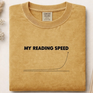 Peut inclure: Un t-shirt à col rond jaune moutarde avec le texte MY READING SPEED imprimé en noir au-dessus d'un graphique linéaire montrant une courbe exponentielle. Le t-shirt présente une étiquette de marque Comfort Colors à l'intérieur du col.