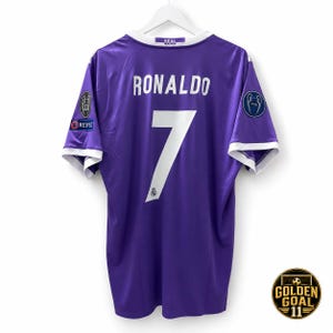 Peut inclure: Un maillot de football violet avec des bordures blanches sur les manches et le col. Le dos affiche le nom RONALDO et le numéro 7 en blanc. Il comprend un logo Real Madrid sur le col, un écusson Respect et un écusson Champions League 2016 sur les manches.