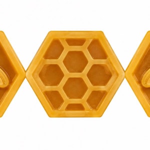 May include: Three hexagonal bars of golden yellow soap arranged in a row. The two outer bars feature a raised relief design of a honeybee centered within the hexagon, while the middle bar displays a raised honeycomb pattern of smaller hexagons.