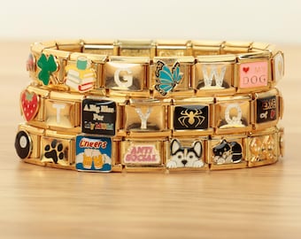 May include: Three gold-tone modular link bracelets featuring various enamel charms including a green clover, stacked books, a blue butterfly, a strawberry, a spider, a dog, and text such as "A Big Kiss For My MOM," "Cheers," and "ANTI SOCIAL."