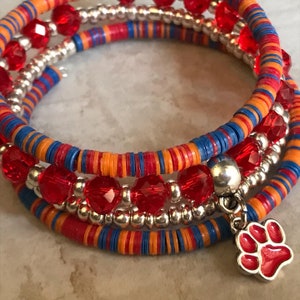 May include: A wrap bracelet with red, orange, and blue accents. The bracelet features red faceted beads, silver beads, and a red paw print charm. The bracelet is made of multiple strands that coil around the wrist.