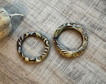 May include: Two ceramic rings with a black and white swirl pattern. The rings are on a wooden surface.