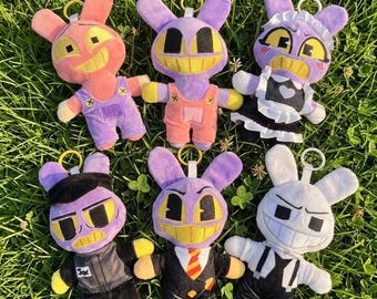 May include: Six plush rabbit keychains with large yellow eyes and wide grins. The top row features a pink rabbit in purple overalls, a purple rabbit in peach overalls, and a purple rabbit in a black and white maid outfit. The bottom row shows a purple rabbit in a black uniform, a purple rabbit in a suit with a striped tie, and a white rabbit in black overalls.