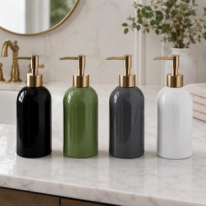 Pode incluir: Um conjunto de quatro dispensadores de sabonete cilíndricos com cabeças de bomba em ouro metálico. Os dispensadores têm acabamento em preto brilhante, verde-oliva, cinza-carvão e branco, cada um com corpo arredondado e bomba funcional.