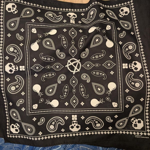 May include: A black bandana featuring a white repeating pattern of pixelated skulls, paisley shapes, and round bombs. The center displays a pixelated anarchy symbol, and the bottom right corner includes the text Property of Dungeon Crawler World.