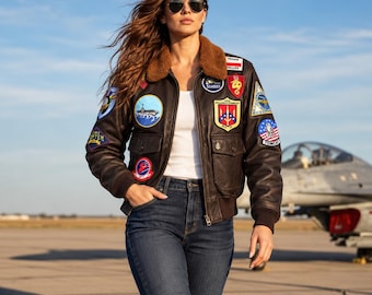 Può includere: Un giubbotto bomber in pelle marrone scuro con colletto in pelliccia sintetica marrone, caratterizzato da numerosi toppe militari ricamate e colorate sul petto e sulle maniche, indossato sopra una canotta bianca e jeans blu scuro con occhiali.