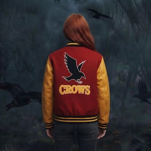 Peut inclure: Une veste universitaire avec un corps en laine rouge foncé et des manches en cuir jaune moutarde. Le dos présente un grand graphique de corbeau noir au-dessus du texte jaune "CROWS" dans une police universitaire. Bordures côtelées rayées.