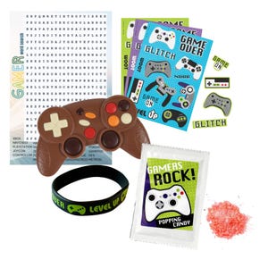 May include: A gamer-themed party favor set with a chocolate game controller, a black silicone bracelet with the words "Level Up" in green, a small packet of popping candy with a green and white game controller graphic and the words "Gamers Rock!" and a sheet of stickers with game controller graphics and phrases like "Game Over", "Glitch", and "Noob".