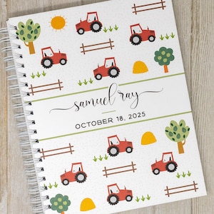 May include: A white spiral bound journal with a red tractor and green tree design. The cover has the text "samuel ray" and "OCTOBER 18, 2025".