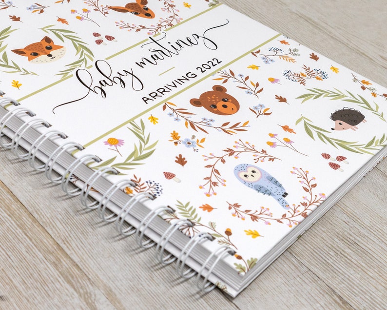 May include: A white spiral bound journal with a woodland animal theme. The cover features a variety of animals including foxes, owls, deer, and hedgehogs. The text on the cover reads "baby martinez arriving 2022".