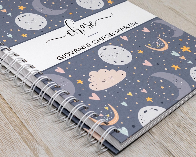 Puede incluir: Un cuaderno gris de espiral con un patr&oacute;n de luna y estrellas. La portada tiene el nombre "chase" escrito en cursiva y el texto "GIOVANNI CHASE MARTIN".