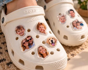 May include: A pair of off-white foam clogs featuring multiple circular ventilation holes. The clogs are decorated with several clear, custom photo charms displaying portraits of children, adults, and a golden retriever dog.