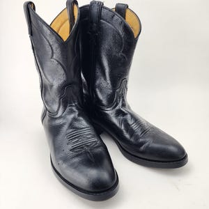 Könnte beinhalten: Ein Paar schwarze Cowboystiefel aus Leder mit klassischer wadenhoher Schaftlänge, spitzer Zehenpartie und Ziernähten an Vorderblatt und Schaft. Die Stiefel verfügen über stabile Anziehschlaufen an den Öffnungen und eine glatte Oberfläche.