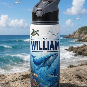 May include: A white water bottle with a dark grey lid featuring a handle. The bottle displays a colourful underwater scene with a blue whale, a sea turtle, a clownfish, a manta ray, and coral. The name WILLIAM is printed in large blue letters.