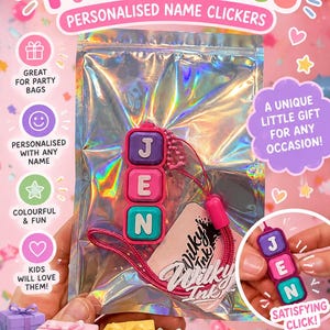 Könnte beinhalten: Ein personalisierter Namens-Klick-Schlüsselanhänger mit drei quadratischen, bunten Kunststoffblöcken, auf denen die Buchstaben J, E und N in Weiß aufgedruckt sind. Der Anhänger ist an einer pinken Schnur befestigt und in einem holografischen Beutel.