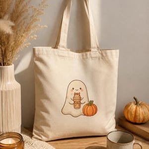 Peut inclure: Un sac fourre-tout en toile de couleur crème arborant un motif central représentant un petit fantôme souriant tenant une tasse de café avec un nœud, à côté d'une citrouille orange. Le sac possède deux longues anses et une forme rectangulaire.
