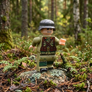 May include: A plastic minifigure wearing a dark gray helmet and a light olive green uniform with brown chest straps, pouches, and red collar tabs. The figure has a printed face with a determined expression and stands on a mossy rock surface.