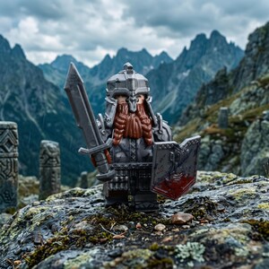 Op de afbeelding: Een plastic minifiguur van een krijger met een lange bruine baard, gekleed in een zilveren helm en harnas. Het figuur houdt een grijs zwaard in de rechterhand en een schild met rode en grijze markeringen in de linkerhand op een rots.