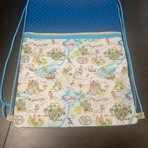 May include: A drawstring backpack featuring a white fabric panel with a colorful treasure map print, including illustrations of castles, ships, and the text My Treasure Map. The top section is blue with white polka dots and light blue drawstrings.