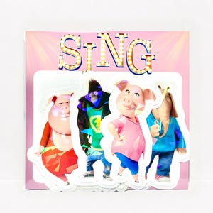 May include: A rectangular card featuring the word SING in marquee-style letters at the top. Below, four die-cut stickers of animated characters are displayed: a pig in a red outfit, a gorilla in a jacket, a pig in a pink shirt, and an elephant.