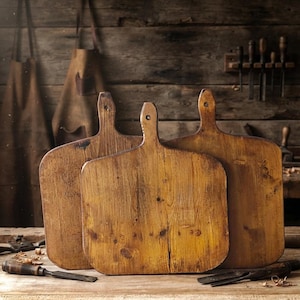 May include: Three rectangular wooden cutting boards with rounded corners and handles featuring a hole at the top. The boards have a natural, weathered brown finish with visible wood grain, knots, and a distressed texture throughout the surfaces.