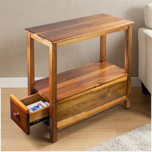 May include: A rectangular wooden side table featuring a smooth top surface, a middle shelf, and a single pull-out drawer at the base. The furniture is constructed from medium-toned wood with visible grain patterns and includes a small round knob.