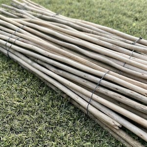May include: A bundle of long, slender, light brown wooden sticks arranged in a parallel formation. The sticks are secured together at intervals by thin, dark metal wire, creating a flexible, rollable structure with a natural, textured finish.